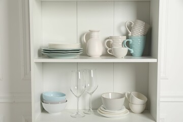 Different clean dishware and glasses on shelves in cabinet indoors