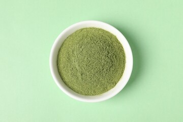 Wheat grass powder in bowl on green table, top view