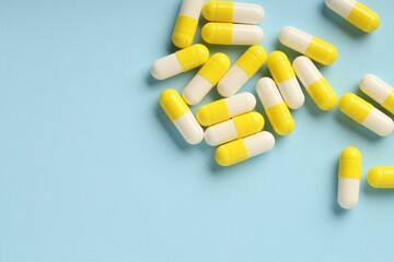 Many antibiotic pills on light blue background, top view. Space for text
