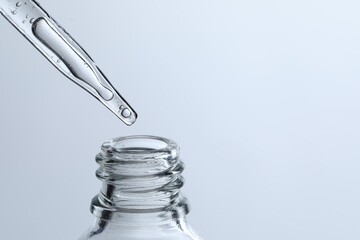 Dripping liquid from pipette into glass bottle on light blue background, closeup. Space for text