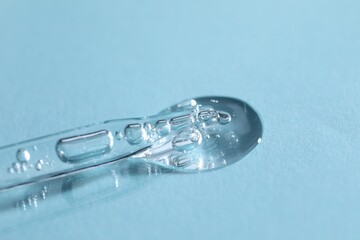 Glass pipette and transparent liquid on light blue background, closeup