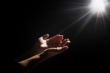 Christian woman stretching hands towards holy light in darkness, closeup. Prayer and belief