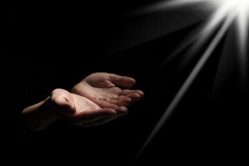 Christian woman stretching hands towards holy light in darkness, closeup. Prayer and belief