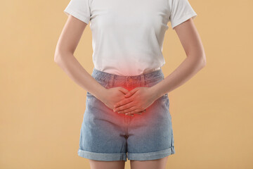 Woman suffering from cystitis symptoms on beige background, closeup