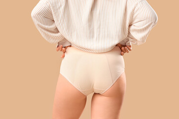 Young woman in period panties on beige background, back view