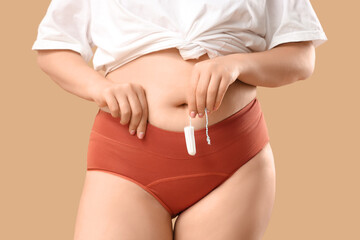 Young woman in period panties holding tampon on beige background
