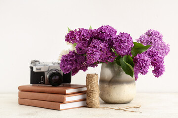 Vase with blooming lilac flowers, books and photo camera on white background