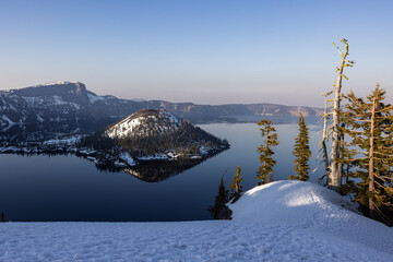 A snowy afternoon in Crater Lake National Park. The lake is calm and reflects wizard Island.