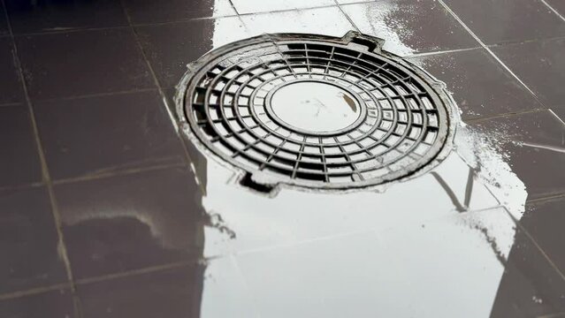 A iron hatch with a pattern and covered water above an observation well is located on pedestrian road in the daytime. Close-up