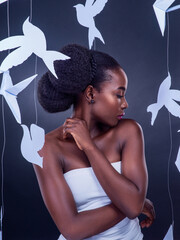 Black woman, paper bird and beauty for freedom, peace and wellness isolated in dark background. African female person and model in studio with makeup, skincare and creative animal art or origami