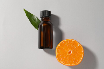 Aromatic tangerine essential oil in bottle, leaf and citrus fruit on grey table, top view