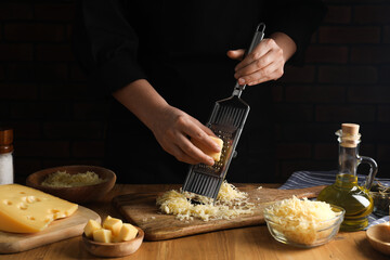 Woman grating cheese at wooden table, closeup - obrazy, fototapety, plakaty