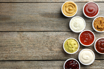 Different tasty sauces in bowls on wooden table, flat lay. Space for text