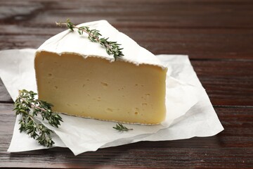 Piece of tasty camembert cheese and thyme on wooden table, closeup