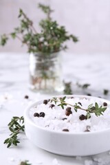 Salt with thyme and peppercorns in bowl on white marble table
