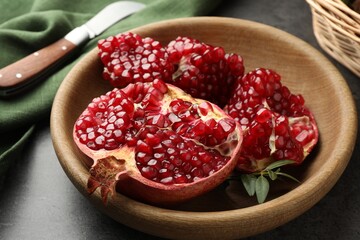 Cut fresh pomegranate, green leaves and knife on grey table, closeup