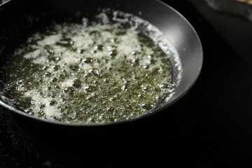 Melting butter in frying pan on black table, closeup