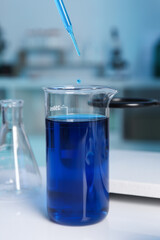 Laboratory analysis. Dripping blue liquid into beaker on white table, closeup