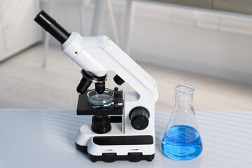 Laboratory analysis. Flask with blue liquid, petri dish and microscope on white table indoors