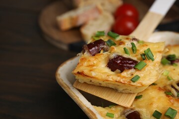 Taking piece of tasty sausage casserole from baking dish at table, closeup. Space for text