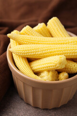 Tasty fresh yellow baby corns in bowl on brown table, closeup