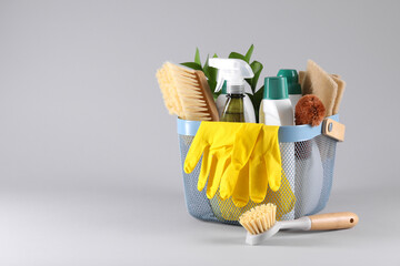 Set of different cleaning supplies in basket on light grey background. Space for text
