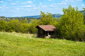 A little house standing in a green field, on top a hill, with the blue sky above