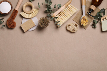 Cleaning brushes, baking soda, soap, sponges and eucalyptus on pale brown background, flat lay....