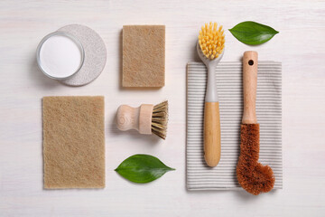 Cleaning brushes, sponges, towel, baking soda and leaves on light wooden table, flat lay