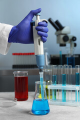 Laboratory analysis. Scientist dripping sample with micropipette into flask indoors, closeup