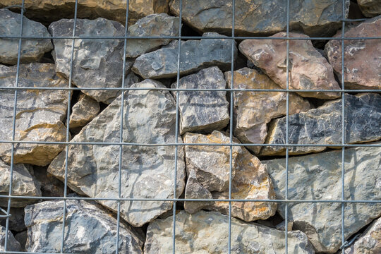 Gray pebbles lie behind a metal grid, a fence made of stones., decorative stones