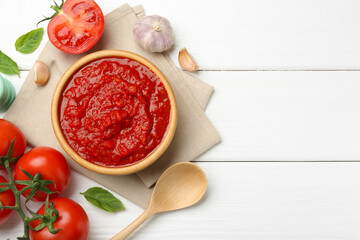 Homemade tomato sauce in bowl, spoon and fresh ingredients on white wooden table, flat lay. Space for text
