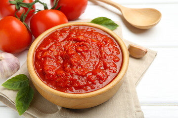 Homemade tomato sauce in bowl, spoon and fresh ingredients on white wooden table, closeup