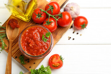 Homemade tomato sauce in jar, spoon and fresh ingredients on white wooden table, flat lay. Space...