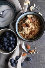 Tasty granola in bowl, blueberries and yogurt on gray textured table, flat lay