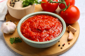 Homemade tomato sauce in bowl and fresh ingredients on light grey table, closeup
