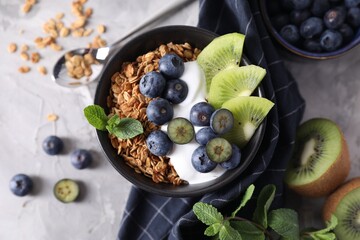 Tasty granola with yogurt, blueberries and kiwi in bowl on gray textured table, flat lay - Powered by Adobe