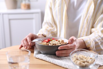 Woman eating tasty granola with banana, cashew and strawberries at wooden table indoors, closeup