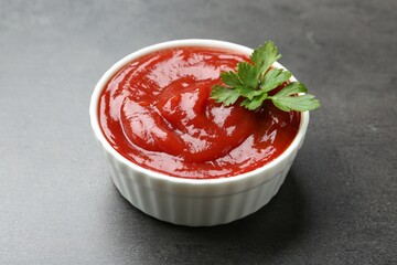 Delicious tomato ketchup and parsley in bowl on grey textured table, closeup