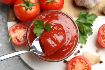 Taking delicious tomato ketchup with spoon from bowl at grey table, top view