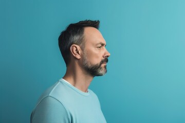 Fototapeta premium A man with a beard and gray hair is wearing a blue shirt and looking away