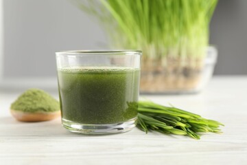 Wheat grass drink in glass and fresh sprouts on white wooden table, closeup