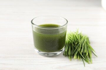 Wheat grass drink in glass and fresh sprouts on white wooden table, closeup