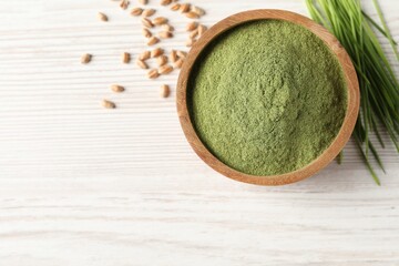 Wheat grass powder in bowl, seeds and fresh sprouts on white wooden table, flat lay. Space for text