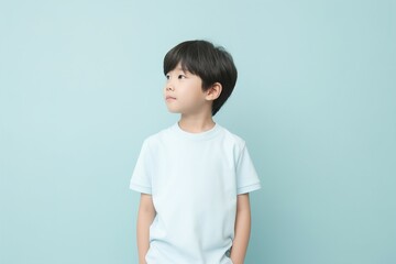 A young boy is standing in front of a blue wall, looking up at the ceiling