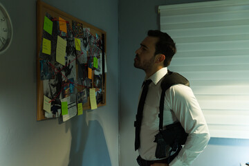 Focused detective stands beside a corkboard covered with investigative clues