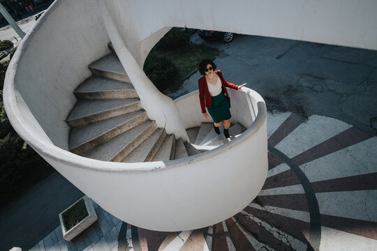 Professional woman in smart attire walking down an outdoor spiral staircase, symbolizing growth and progress.