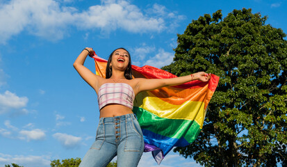 mujer joven hispanoamericana al aire libre en verano ondeando la bandera del orgullo gay 