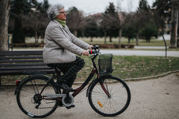 Obraz premium Mature woman enjoying her retirement with a leisurely bicycle ride in a serene park setting.