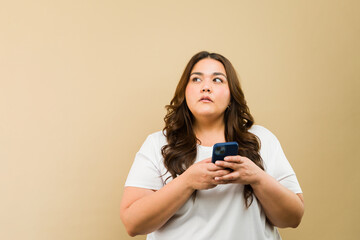 Thoughtful plus-size woman holding a phone, gazing towarads copy space in a studio setting